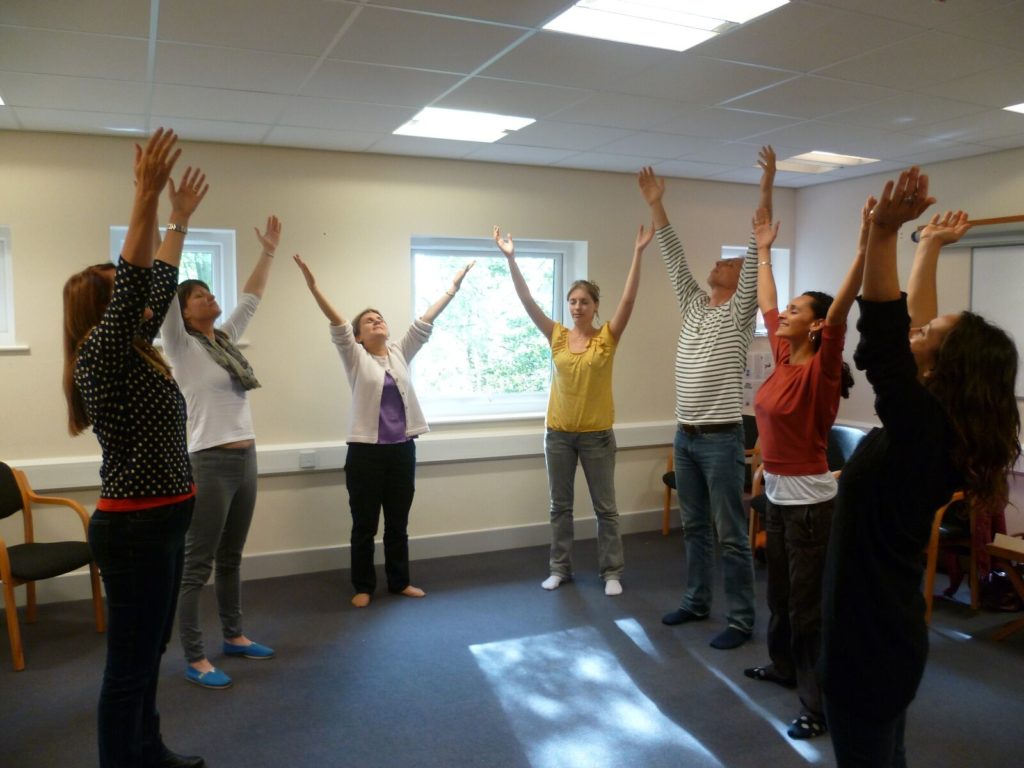 A sophrology group standing with arms raised during a session